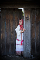 A woman in a Russian folk dress and a scarf standing at the wooden gate