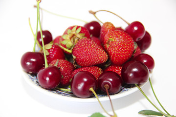  red berries of strawberries and burgundy cherries with green leaves on a plate isolated on white background