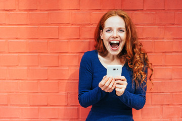 frau mit mobiltelefon steht vor einer roten wand und freut sich 