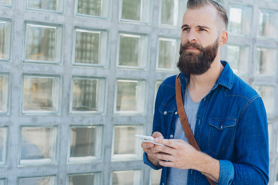Serious bearded man standing holding a mobile