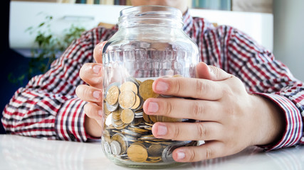 Closeup photo of young man holding glass jar full of coins