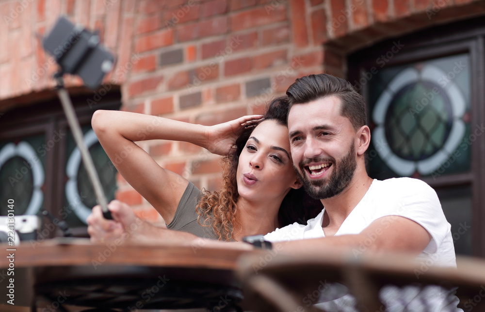 Poster Happy cheerful couple sitting down at a cafe and making selfie