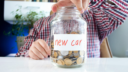 Closeup image of young man holding glass jar with money saving for buying new car