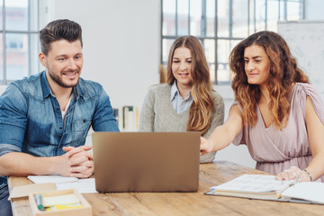 team im büro sitzt am besprechunngstisch und schaut auf laptop