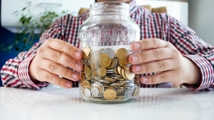 Closeup image of young man holding glass jar full of coins