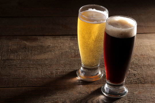 A glass of light and a glass of dark beer on a wooden brown background with a place for an inscription