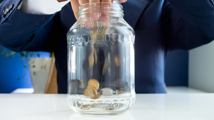 Closeup photo of young businessman throwing coins in glass jar