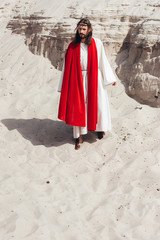 Jesus in robe, red sash and crown of thorns walking in desert