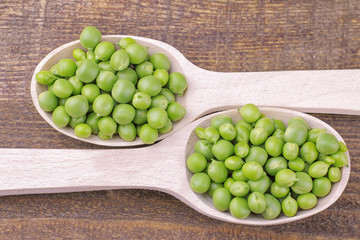 Fresh green peas in wooden spoons close-up on a brown wooden table. top view