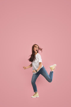 Freedom in moving. Mid-air shot of pretty frightened running away young woman jumping against pink studio background. Runnin girl in motion or movement. Human emotions and facial expressions concept