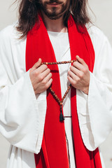 cropped image Jesus in robe and red sash holding wooden rosary in desert