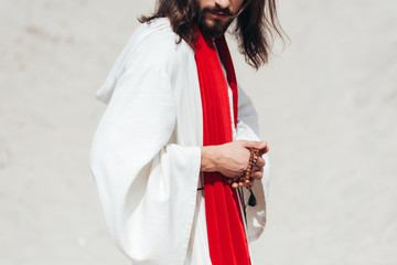 cropped image Jesus in robe and red sash holding rosary in desert
