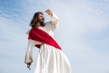 Jesus in robe, red sash and crown of thorns holding rosary and protecting face from light in desert