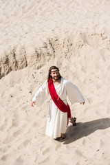 high angle view of Jesus in robe, red sash and crown of thorns walking on sand in desert