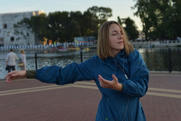 Young woman in headphones in the evening dancing on the street