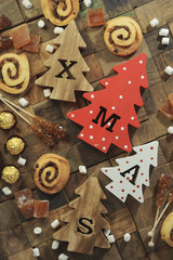 Four decorative wooden Christmas trees with carved letters xmas and christmas sweets. Top view.