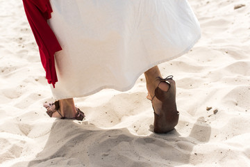 cropped image of Jesus in robe, sandals and red sash walking on sand in desert - Powered by Adobe
