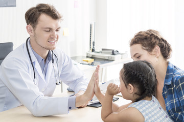 Obraz premium Pediatrician (doctor) man giving fist bump (High Five To),reassuring and discussing kid at surgery.Mother Caucasian and kid smiling in hospital room.Copy space.