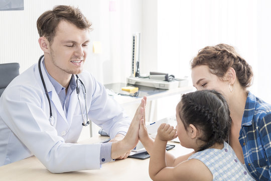 Pediatrician (doctor) man giving fist bump (High Five To),reassuring and discussing kid at surgery.Mother Caucasian and kid smiling in hospital room.Copy space.