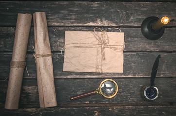 Blank letter page, magnifying glass, burning candle and feather pen on wooden desk background.