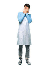 A full-length shot of a Man wearing an apron covering eyes by hands and looking through the fingers on isolated background