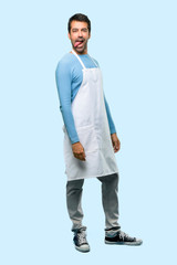 Full body of Man wearing an apron showing tongue at the camera having funny look on blue background