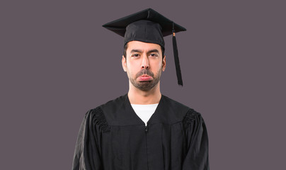 Man on his graduation day University with sad and depressed expression. Serious gesture on violet background