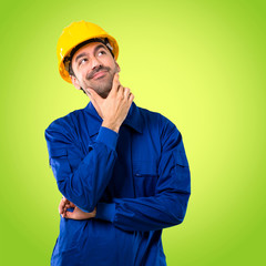 Young workman with helmet standing and thinking an idea on green background