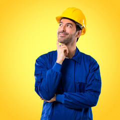 Young workman with helmet standing and thinking an idea while looking up on yellow background