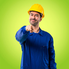 Young workman with helmet points finger at you with a confident expression on green background