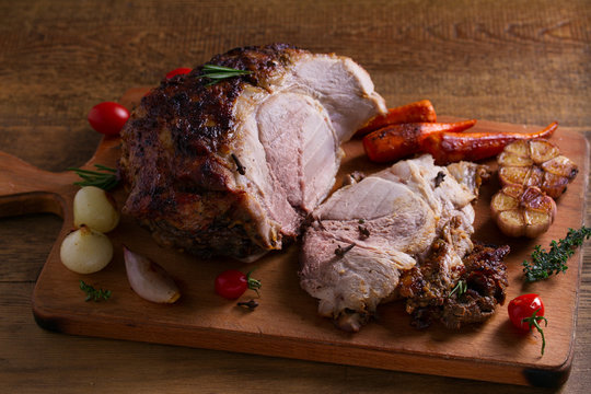 Baked ham with vegetables: carrots, onions, tomatoes, garlic and herbs on chopping board