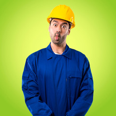 Young workman with helmet makes funny and crazy face emotion on green background