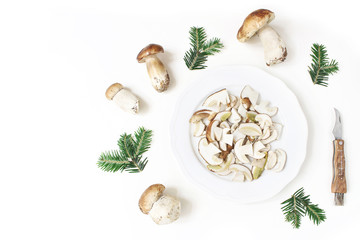 Autumn styled food arrangement. Composition of whole and sliced porcino mushrooms, Boletus edulis on white plate, fir branches and pocket knife. White table background. Fall design, flat lay, top view