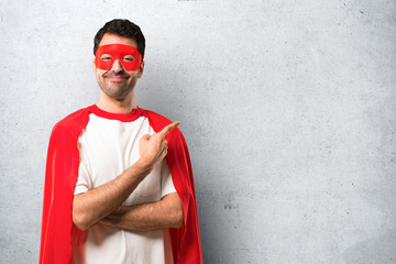 Superhero man with mask and red cape pointing to the side with a finger to present a product or an...