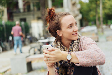 friendly woman sitting on a bench holding her smart phone