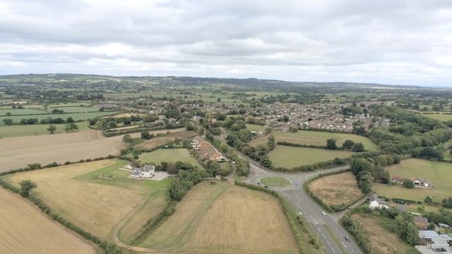 Aerial view, down and panning move. Cars on roundabout, houses and yellow stubble fields in Cheshire.