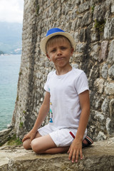boy in a blue hat sitting on parapet of the ancient fortress of Old town in Budva, Montenegro