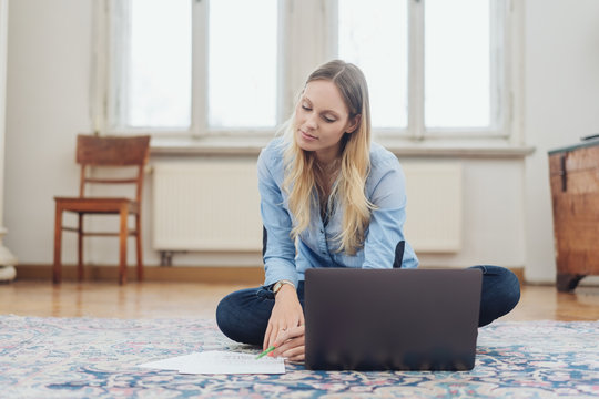 Blonde woman sitting on carpet with laptop
