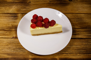 Piece of tasty New York cheesecake with raspberries in a white plate on wooden table