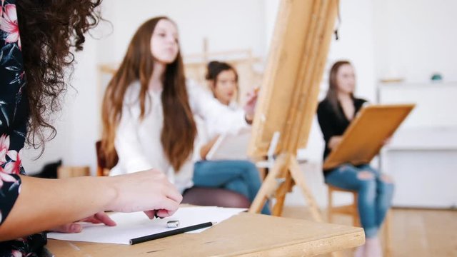 Attractive girls are sitting behind the easel close up hands