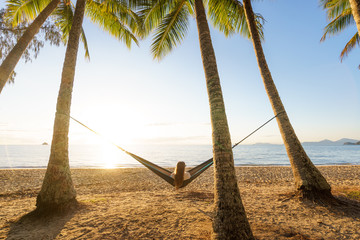 Woman on hammock amongst palm trees on a beach