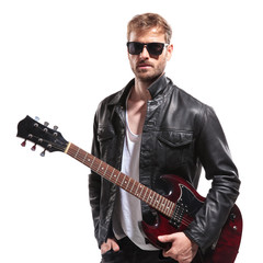 attractive man standing with hand in pocket while holding guitar