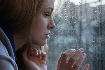 sad young woman looking through window on rainy day. depression concept.