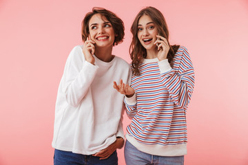 Fototapeta premium Women friends isolated over pink wall background talking by mobile phones.