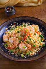 Shrimps with couscous, green peas, leeks and carrot. vertical