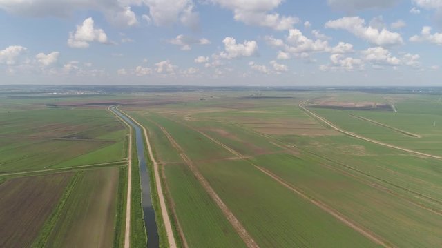 Aerial view of agricultural, cultivated fields with irrigational channel. Agricultural landscape rows. Irrigated farmland. Countryside with fields of crops.