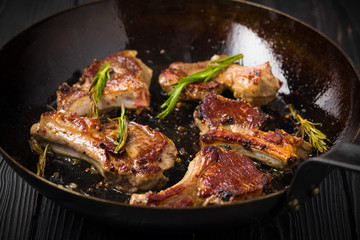 Lamb chops frying in a rustic metal pan with rosemary and mixed pepper © Kirill