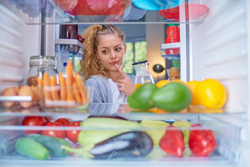 Woman standing in front of opened fridge and choosing what to eat for breakfast. Fridge full of groceries.
