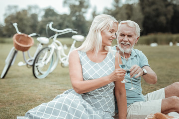 Cheers. Joyful mature couple spending time together in park while having romantic picnic