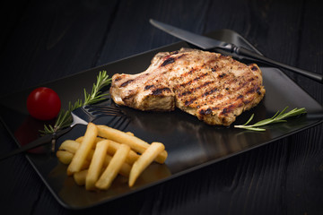 Grilled pork steak on a black plate served with french fries and rosemary